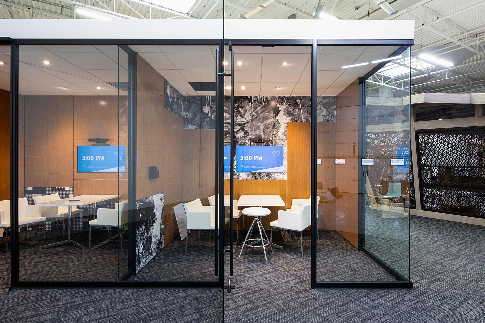A free standing group of offices with glass walls, black trip, and wood separating and back walls.