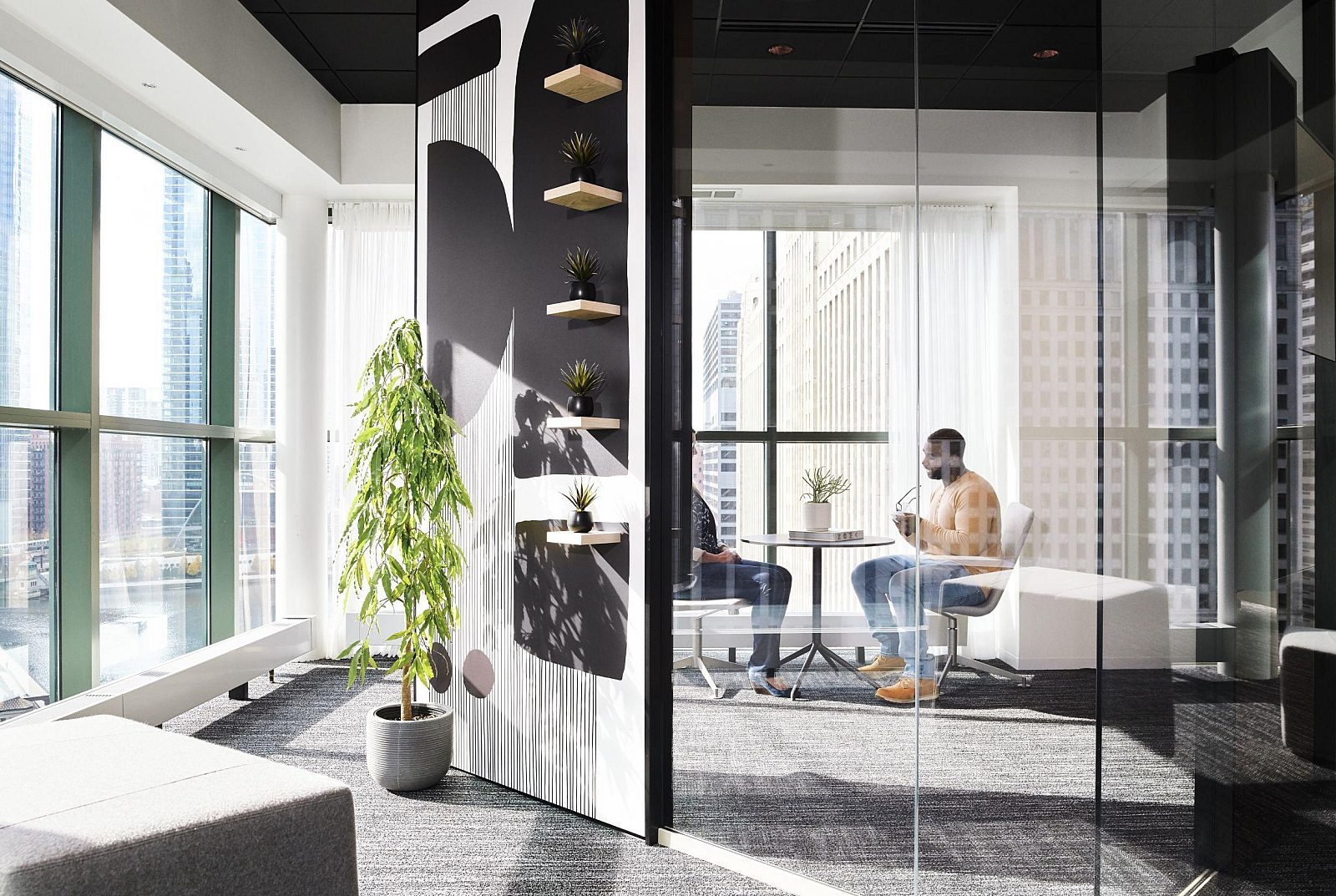 A glass wall with invisible butt joins, with a reflection showing people seated in an office.