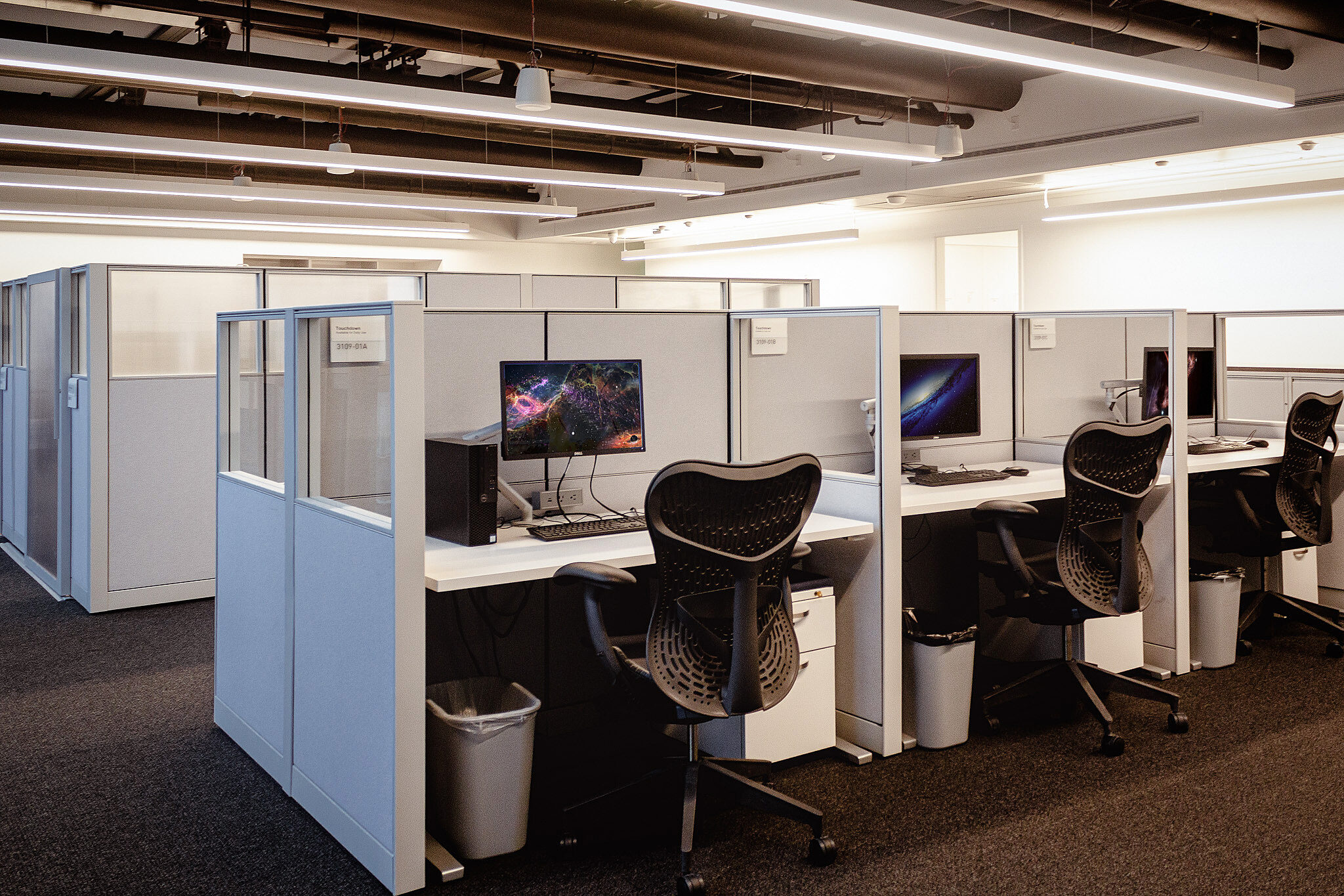 A cluster of small workstations with fabric and glass panels separating them